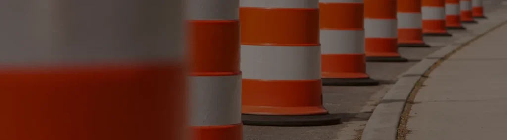 Close-up row of orange and white safety barrels lining the edge of a roadwork zone